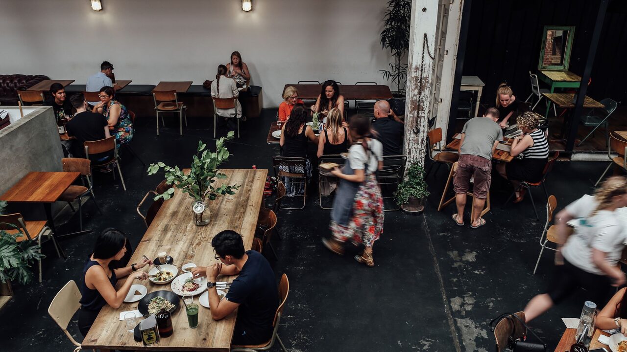 Wide dining room of an established restaurant, slatted wood ceiling, tables laid and warm evening light