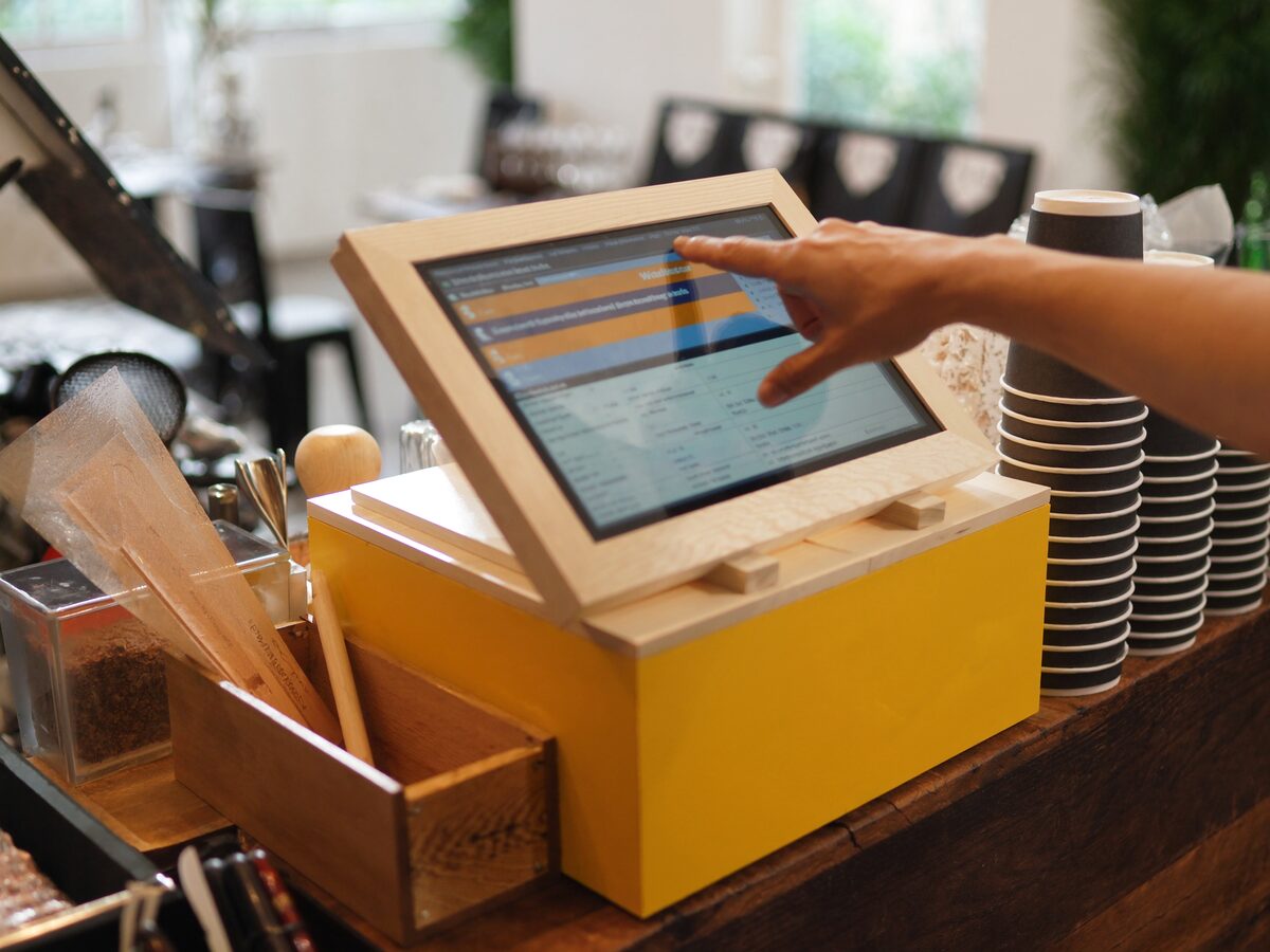 Mano cobrando un pedido en la pantalla táctil del punto de venta, mostrador de una cafetería