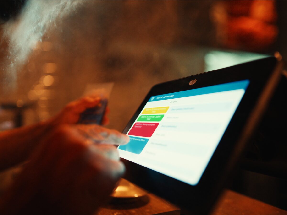 Mano tocando la pantalla del punto de venta en el mostrador de una pizzería